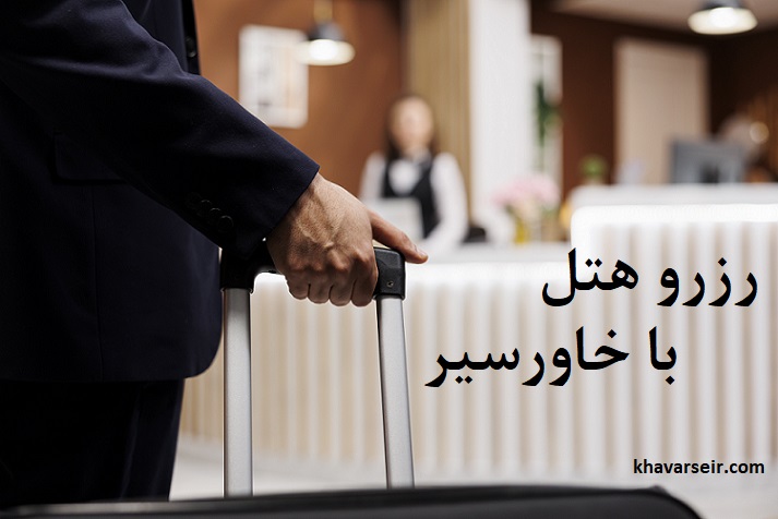 تصویر پس زمینه کمی تار از ایستگاه پذیرش هتل و در جلوی تصویر مردی با کت شلوار که چمدانی در دست دارد